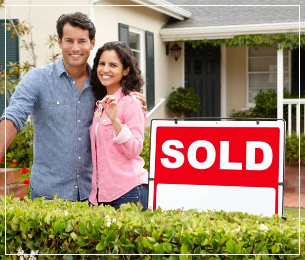 Hispanic couple outside home with sold sign